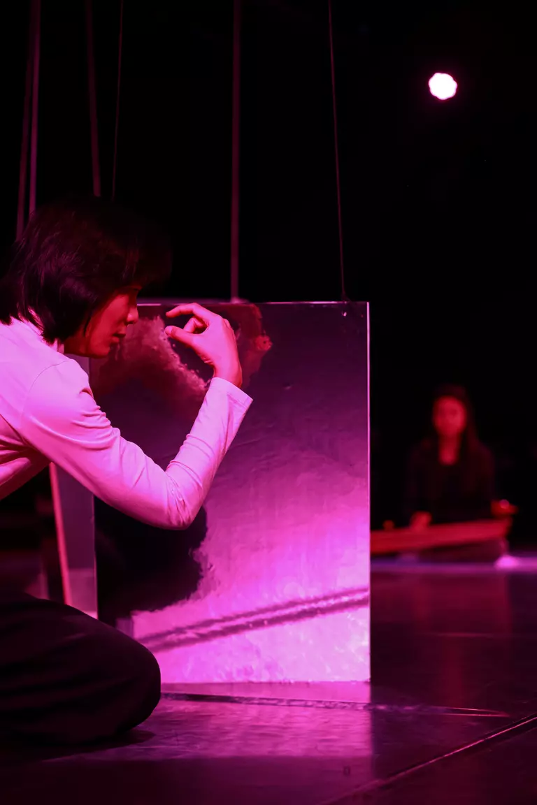 Die Tänzerin Trần Minh Hải sitzt in lila Licht am Boden und ist einer spiegelnden Fläche zugewandt.